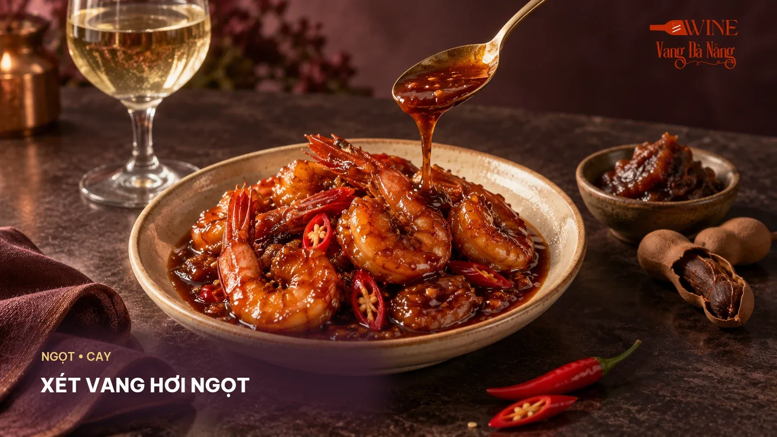 Tôm rim sốt sẫm sánh với ớt, me, muỗng sốt và ly vang trắng ở phía sau